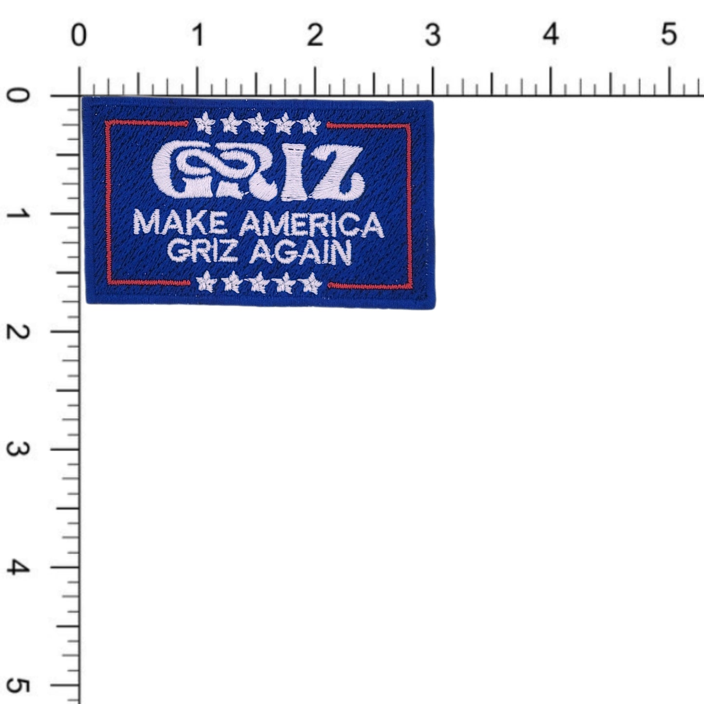 "Make America Griz Again" embroidered patch/iron-on applique. Parodies infamous political campaign moto. Blue background with white text and stars and a red border. Shown against a ruler to demonstrate size- 3.00 inches x 1.75 inches