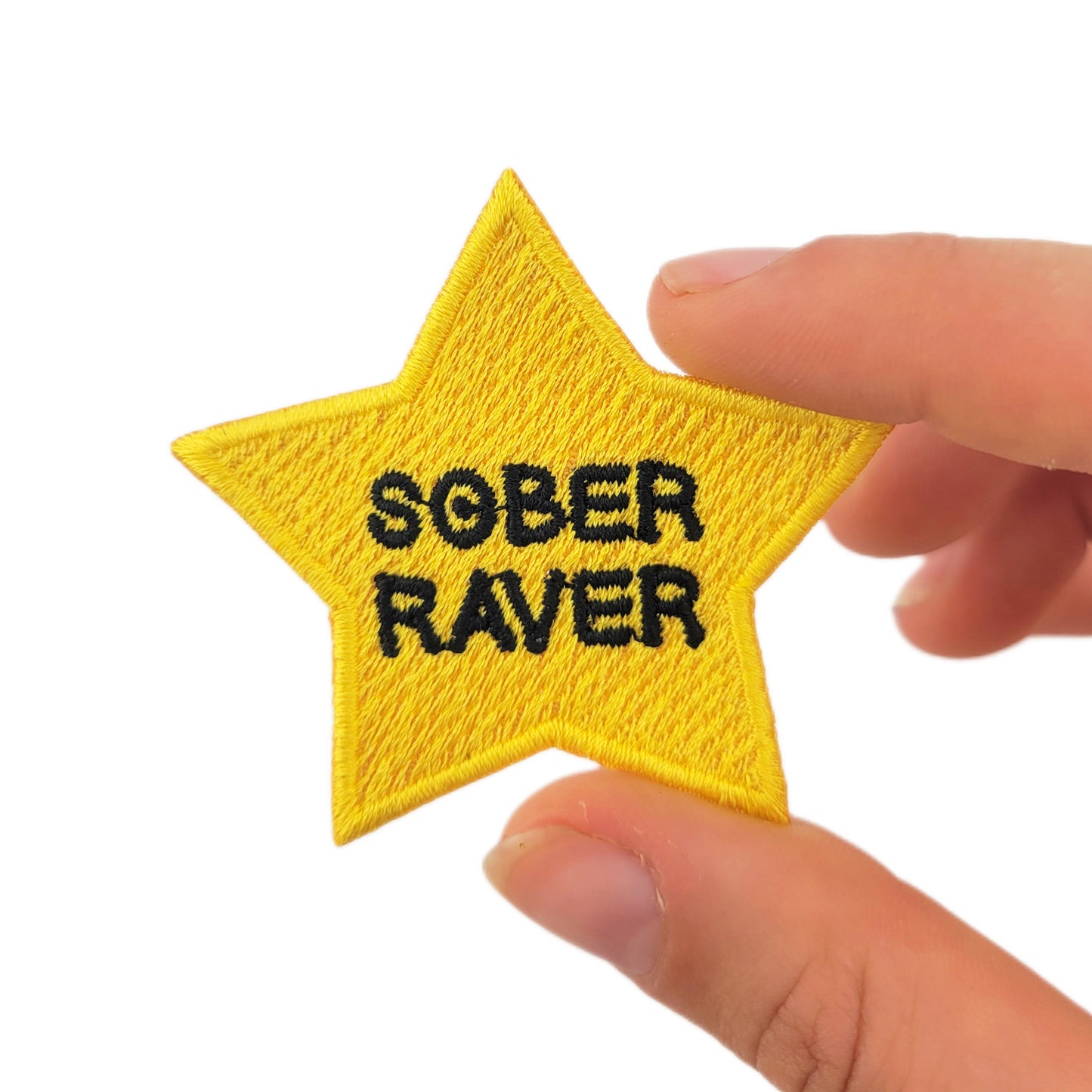 Yellow star patch with 'SOBER RAVER' text held by a hand on a white background