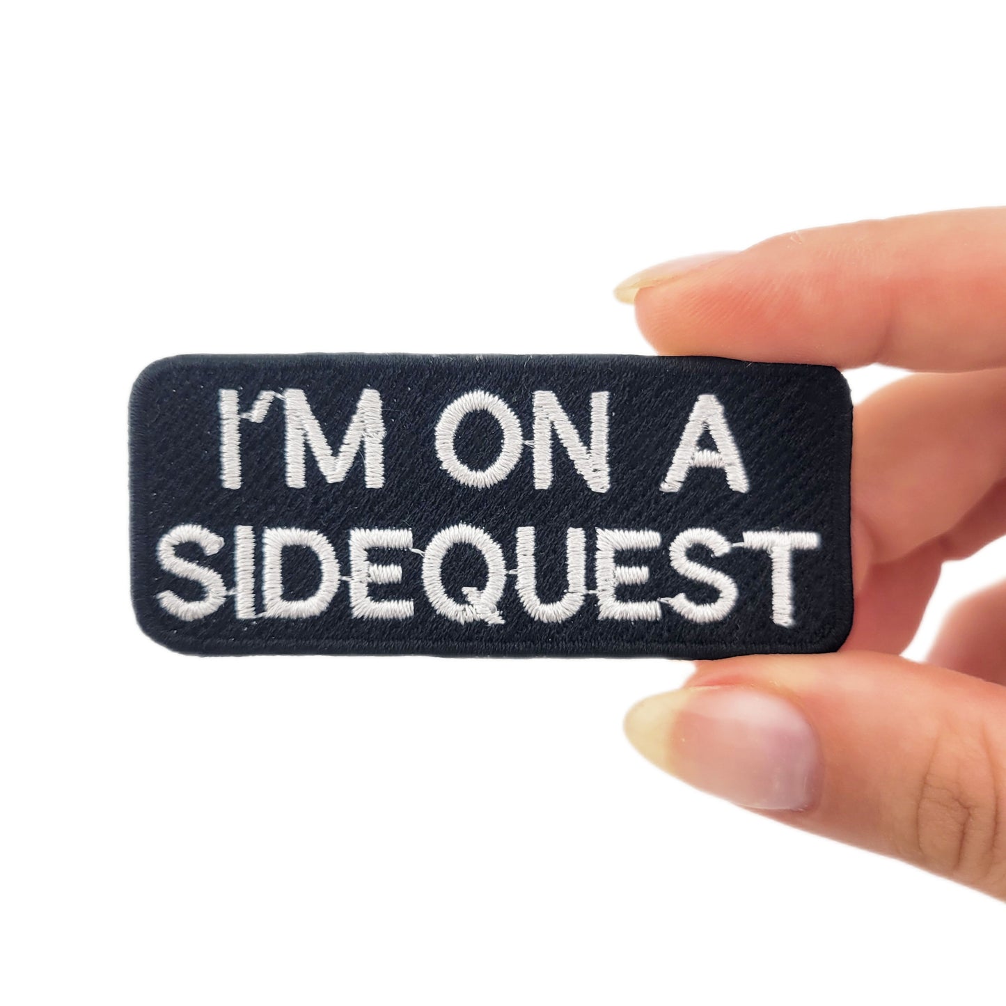 Embroidered patch with 'I'm on a sidequest' text held by a hand on a white background