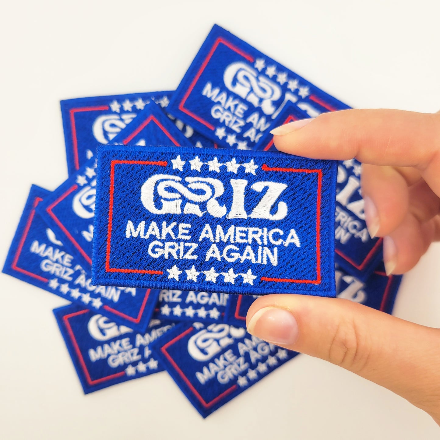 "Make America Griz Again" embroidered patch/iron-on applique. Parodies infamous political campaign moto. Blue background with white text and stars and a red border.