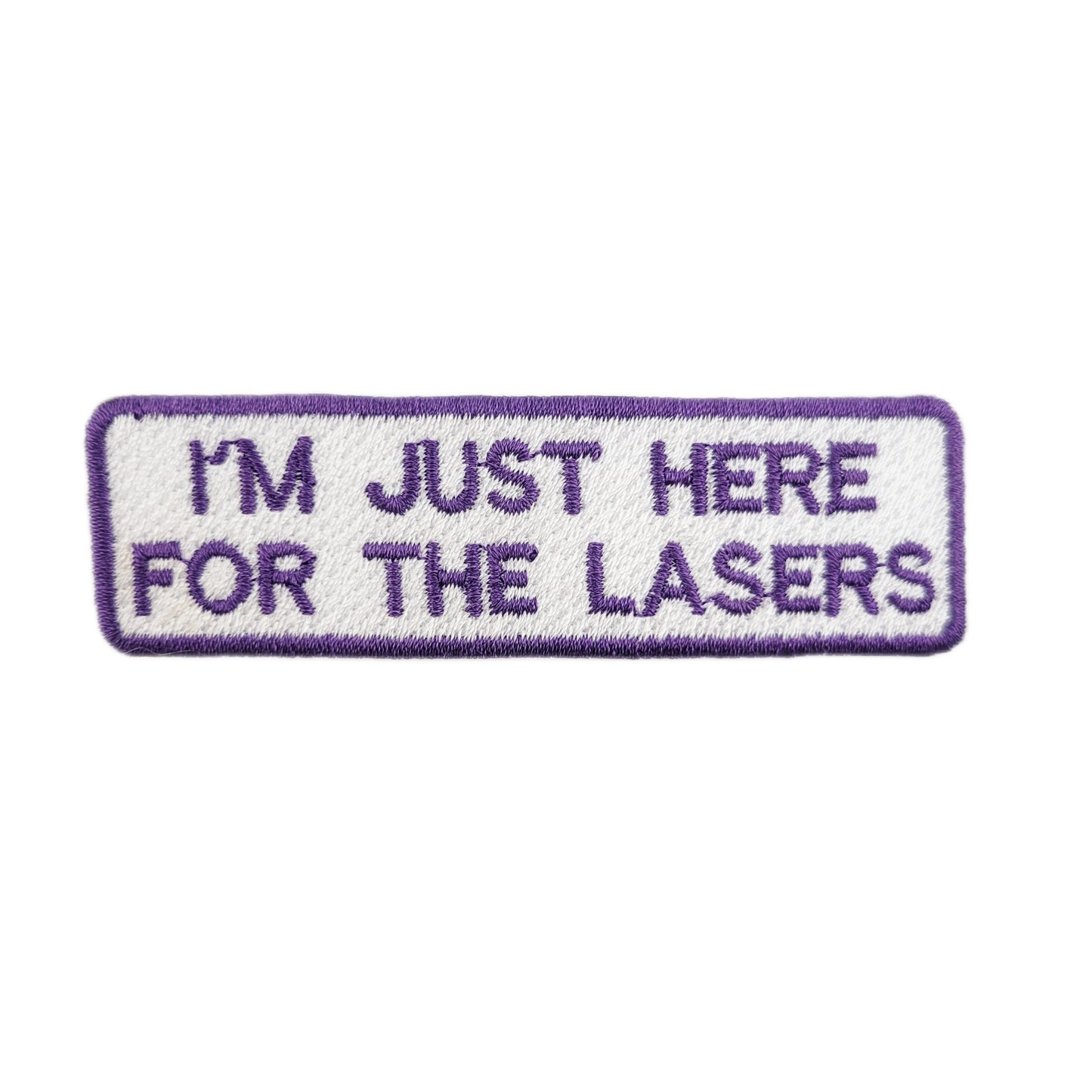 Embroidered patch with text 'I'm just here for the lasers' written in purple text on a white background