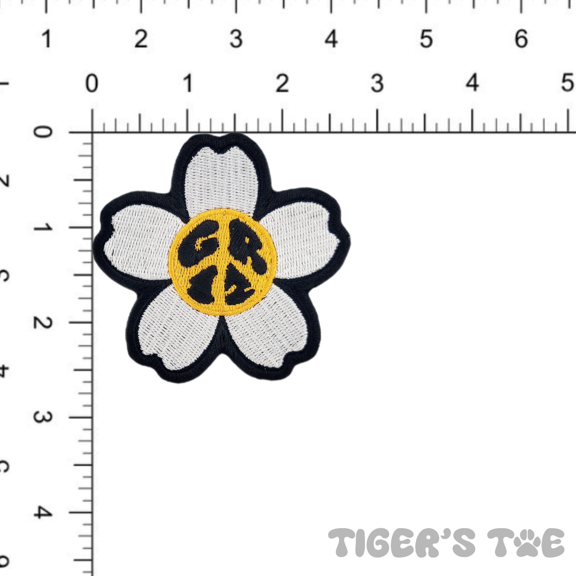 Embroidered patch of a 5-petal white daisy with a yellow center. The center also spells out "GRiZ" in the shape of a peace sign, hence the name "GRiZ Peace Daisy". The Patch in shown next to a ruler to demonstrate size, approximately 2.85 x 2.75 inches.