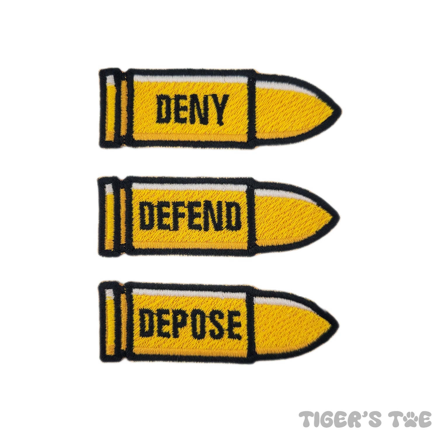 3 bullet-shaped yellow embroidered patches with the text "deny, defend, depose" written on each one, respectively. Displayed on a white background.