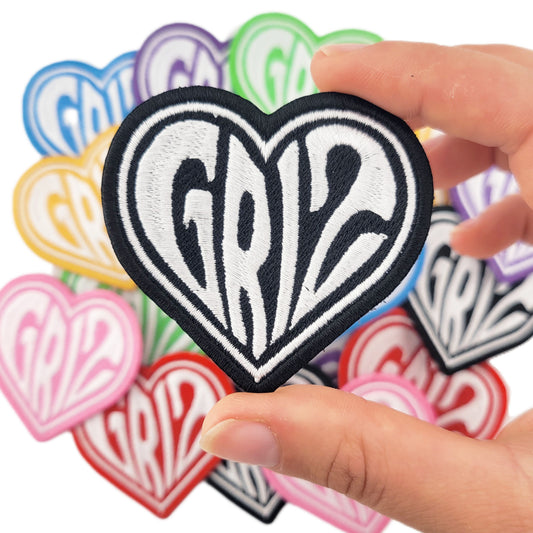Heart-shaped patch with 'griz' text held by a hand against a background of similar patches.