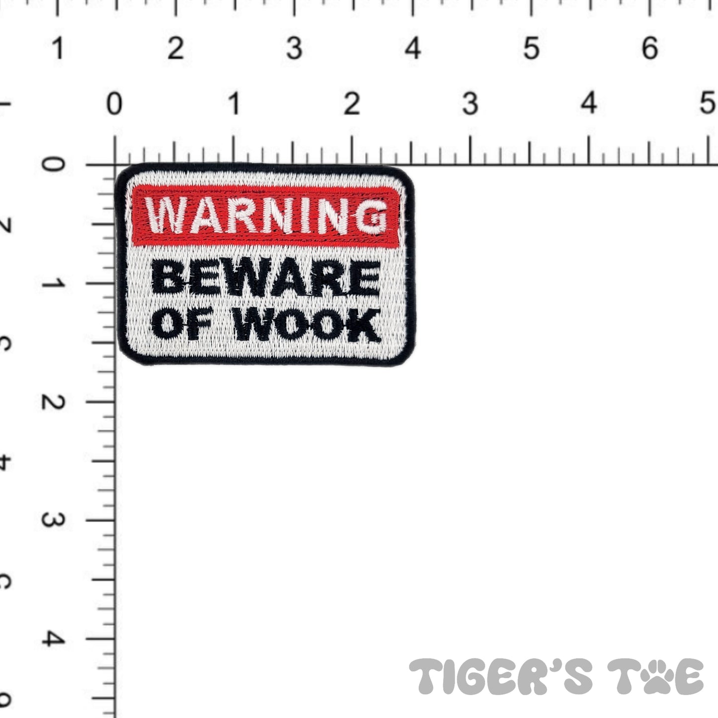 embroidered patch in the design of a warning sign that reads 'warning beware of wook' against a ruler for scale