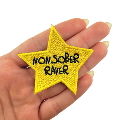 Yellow star patch with 'NON SOBER RAVER' text held in a hand on a white background