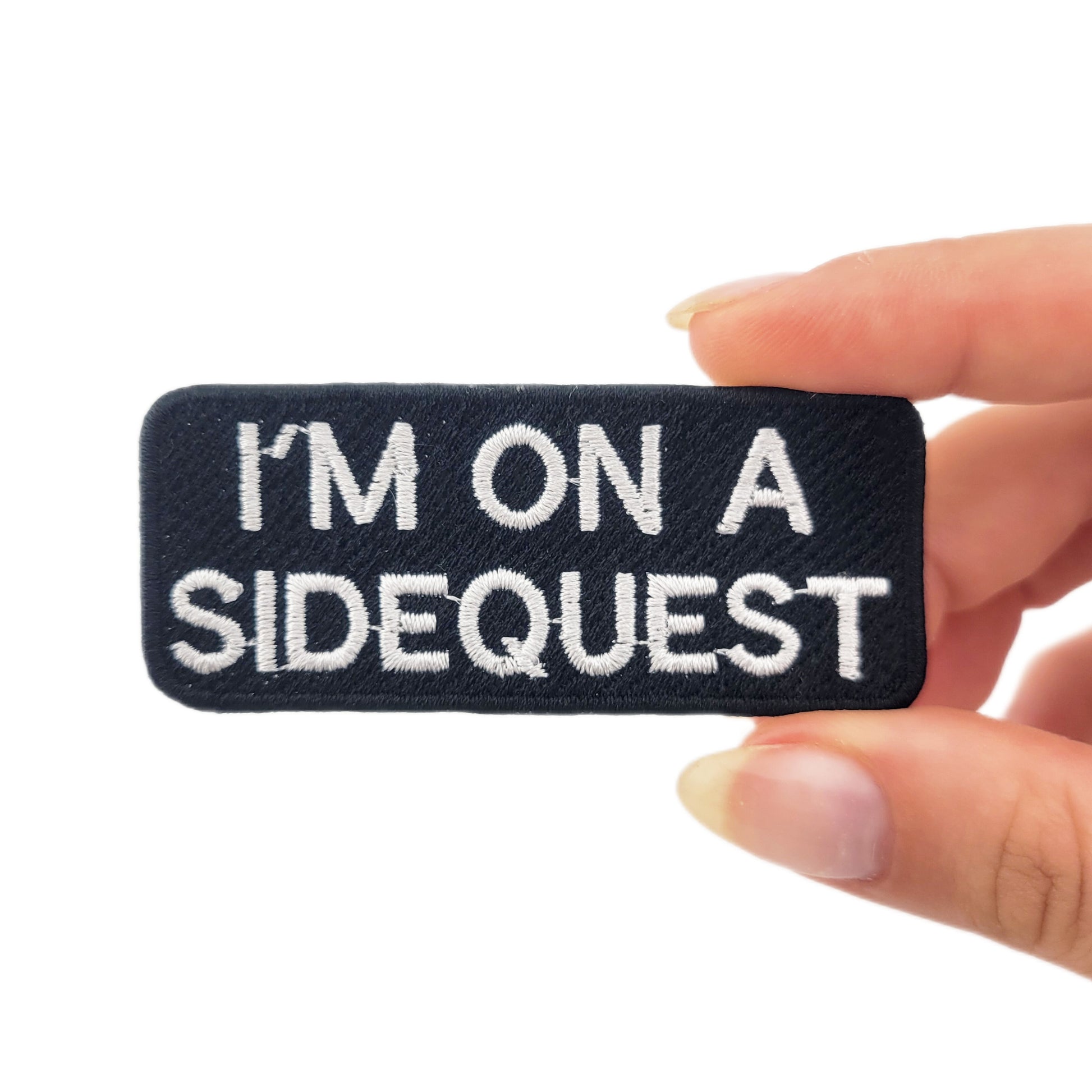 Embroidered patch with 'I'm on a sidequest' text held by a hand on a white background