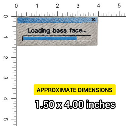 Textile patch with 'Loading bass face...' design on a ruler for scale, showing dimensions.