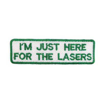 Embroidered patch with text 'I'm just here for the lasers' written in green text on a white background