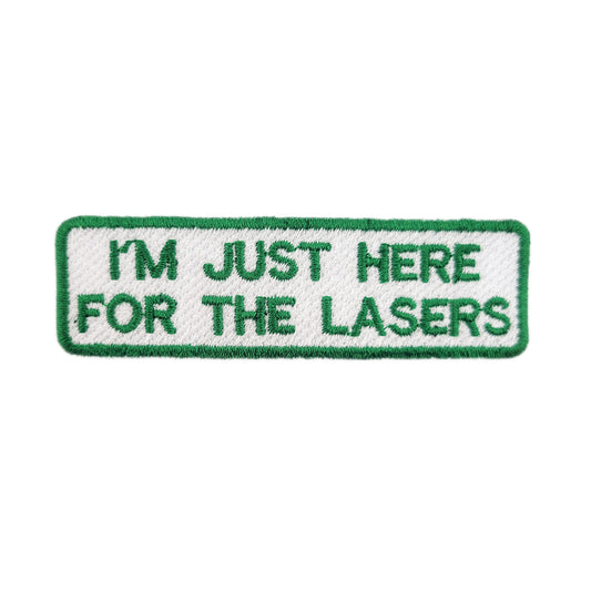 Embroidered patch with text 'I'm just here for the lasers' written in green text on a white background
